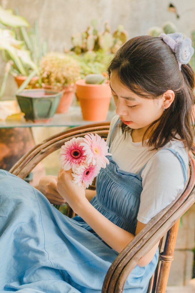 A girl sitting in a chair holding a flower