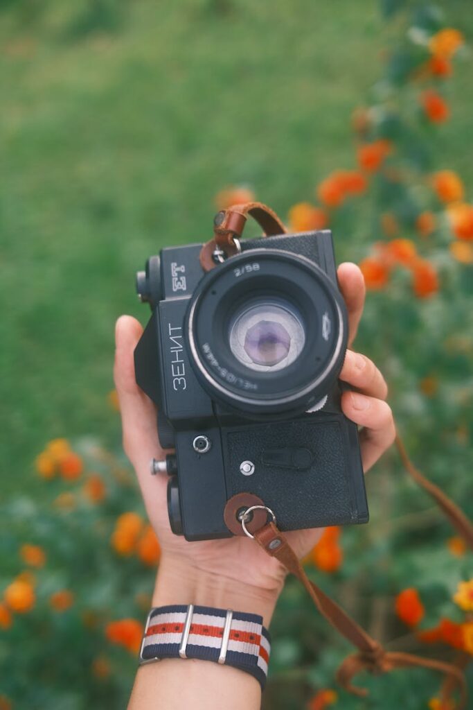 A person holding an old camera in front of flowers