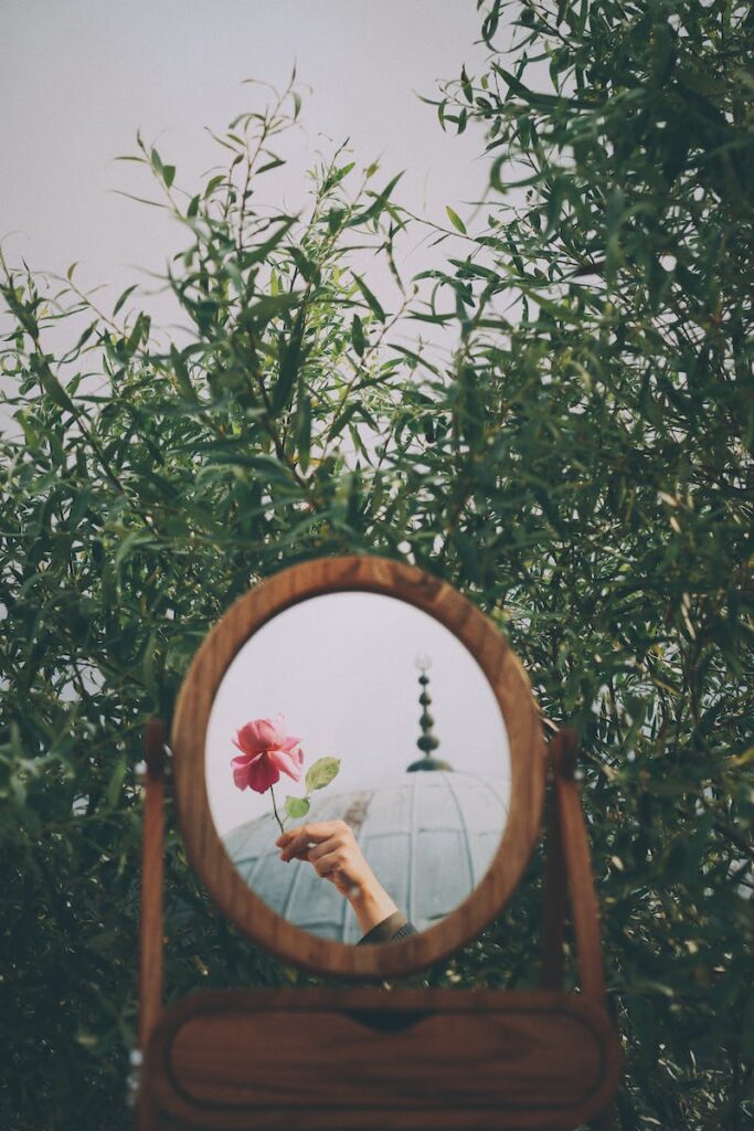 Reflection of a Person Holding a Flower in a Mirror of a Dresser Standing Outside