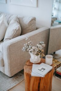 Cozy sofa with decorative cushions near stump with books and blooming flowers in vase in house room