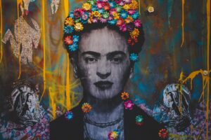 Creative artwork with Frida Kahlo painting decorated with colorful floral headband on graffiti wall