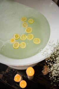 From above of white tub with clear water near burning candles and blooming flowers in modern bathroom during skincare treatment