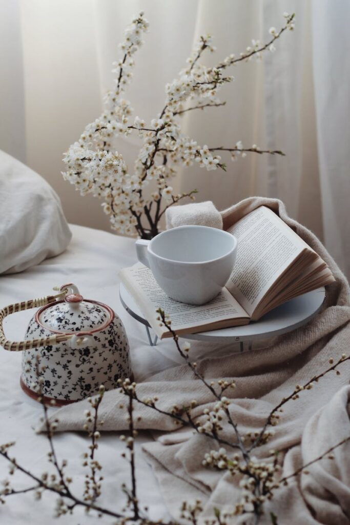 Elegant composition of teapot and cup placed on bed with book